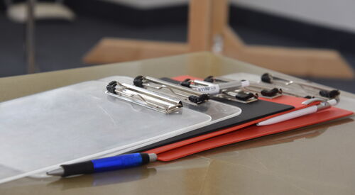 Klemmbretter, darauf ein Stift und ein Kugelschreiber, liegend auf einer Tischfläche.